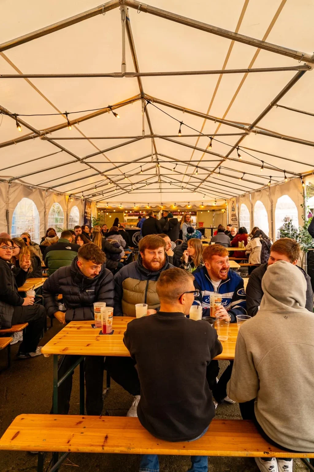 Crowds seated at long benches inside a marquee at an Eat Street Cumbria event, enjoying food and drinks.