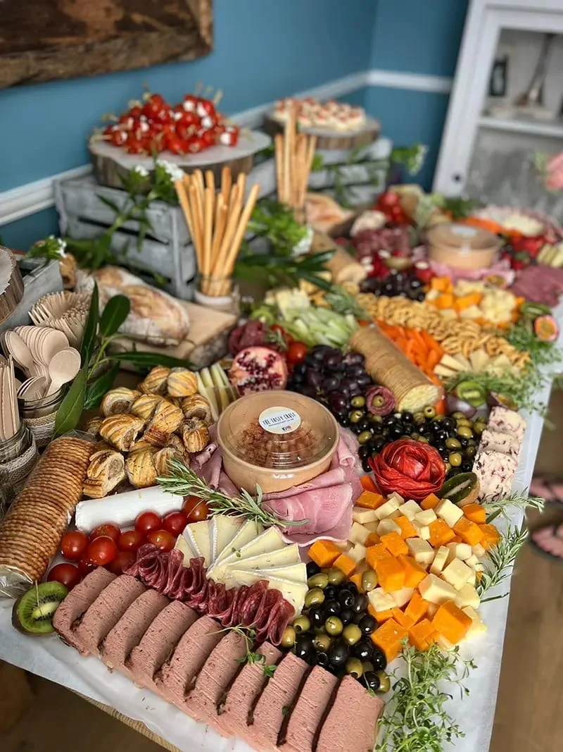 A large grazing table filled with meats, cheeses, breads, pastries, crackers, fruits, dips, and vegetables arranged decoratively across a long table.