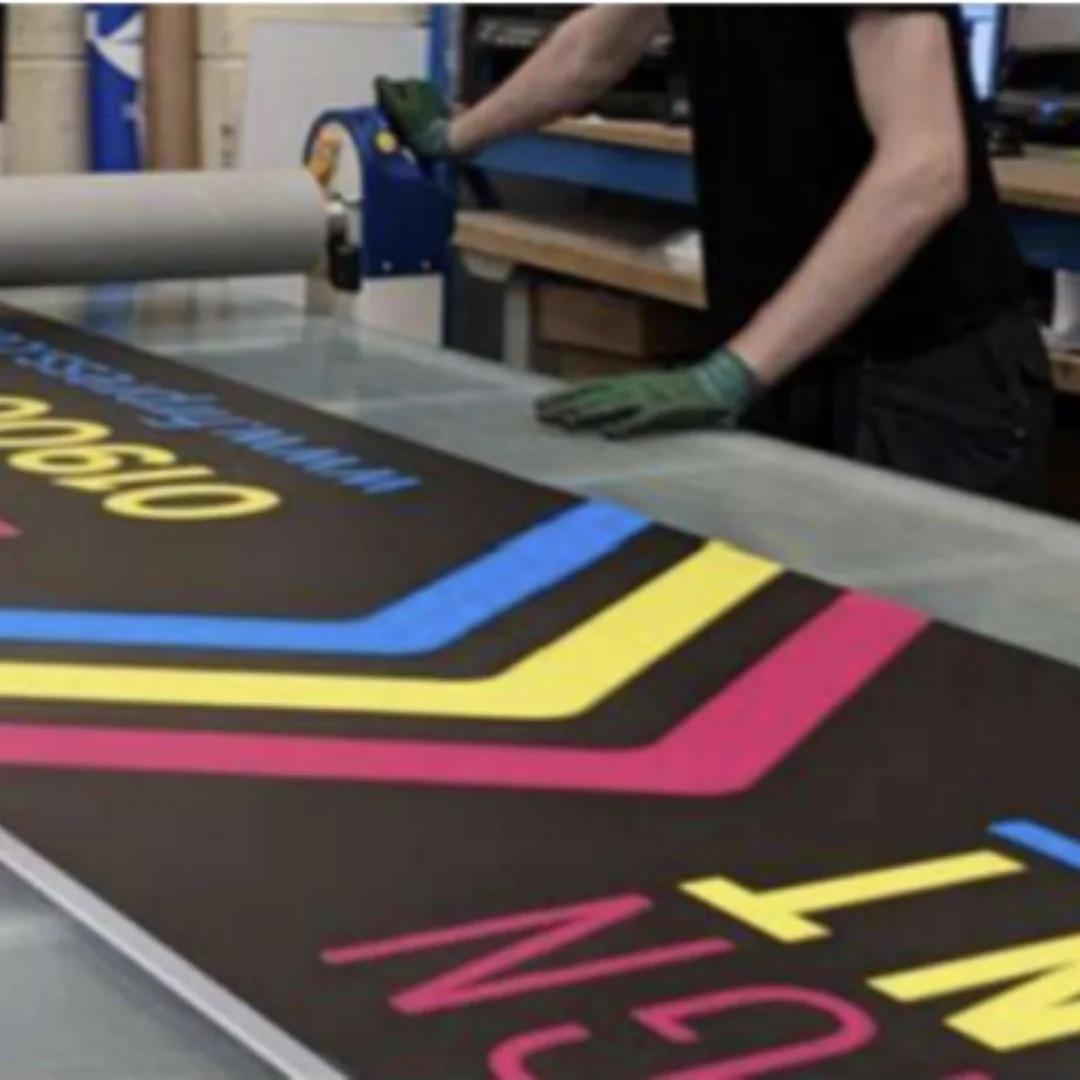Person handling a large printed banner on a worktable inside a print and signage workshop