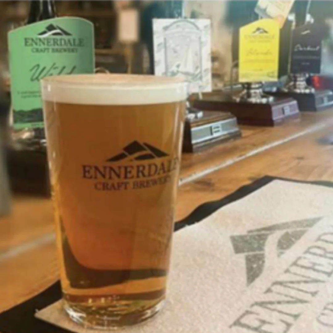 A pint of Ennerdale craft beer on a bar counter with brewery pump clips in the background.