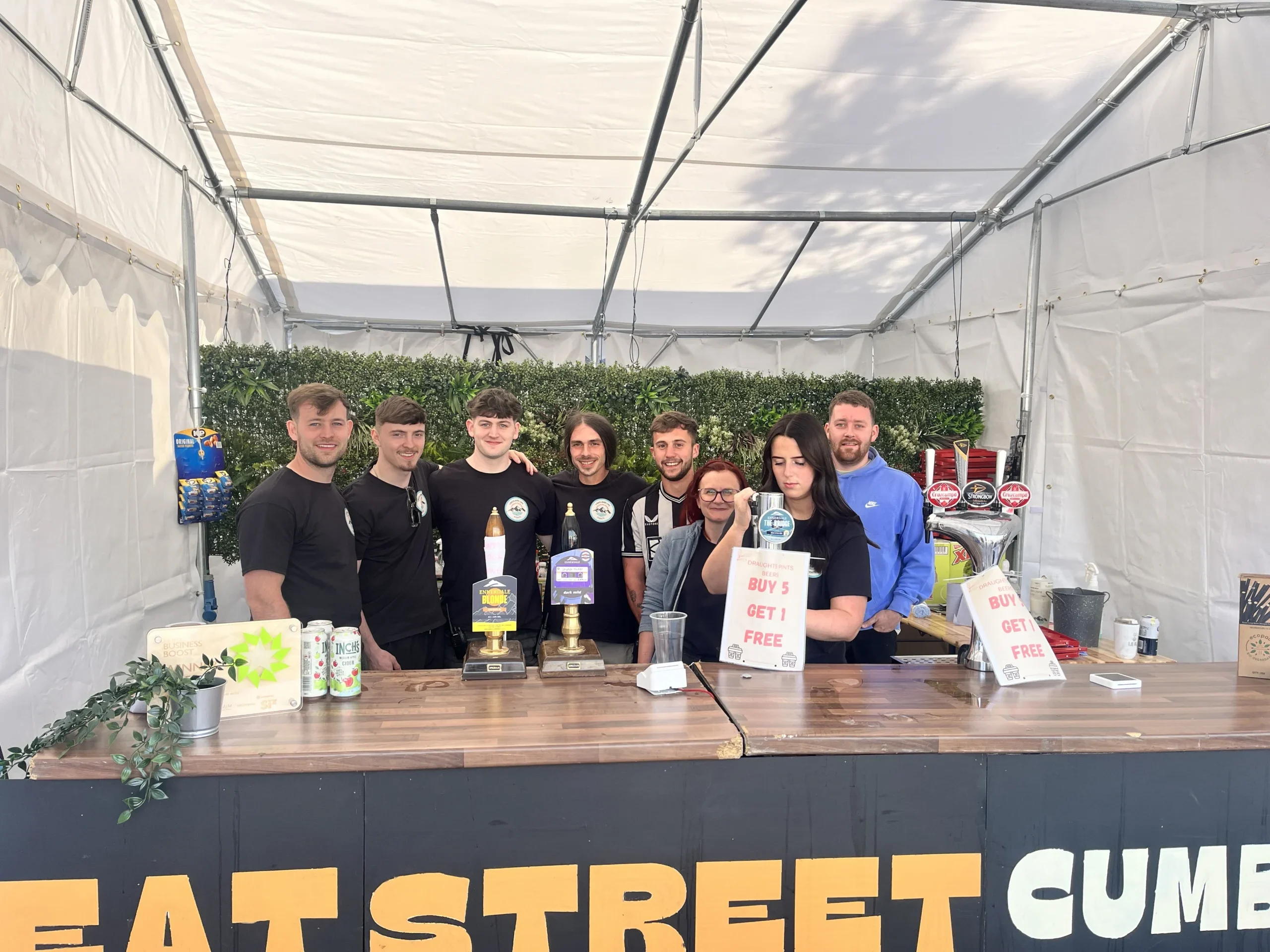 Event bar team posing behind the counter at an outdoor marquee bar.