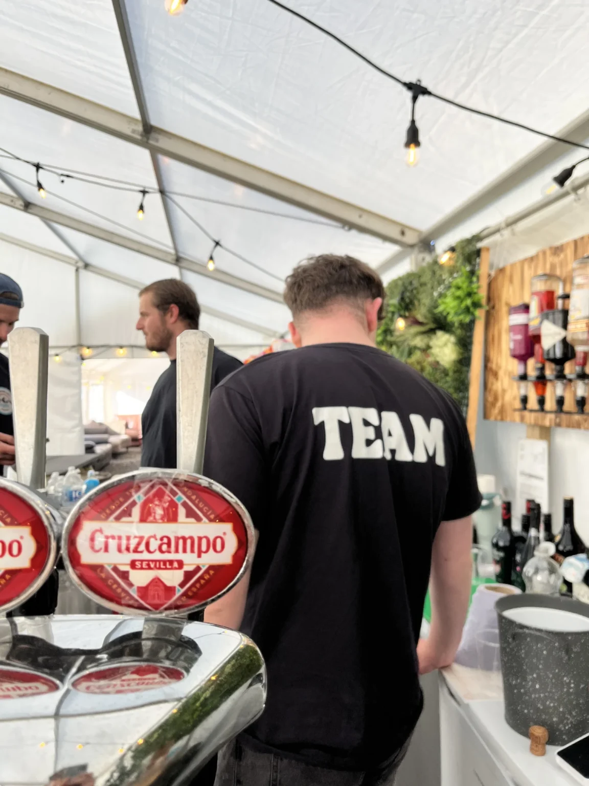 Bar staff working behind a beer tap inside an event tent.